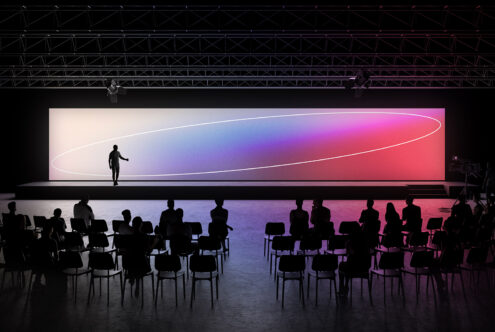 Silhouetted speaker on stage at a modern conference with dynamic gradient lighting and attentive audience for event mockup design presentations.